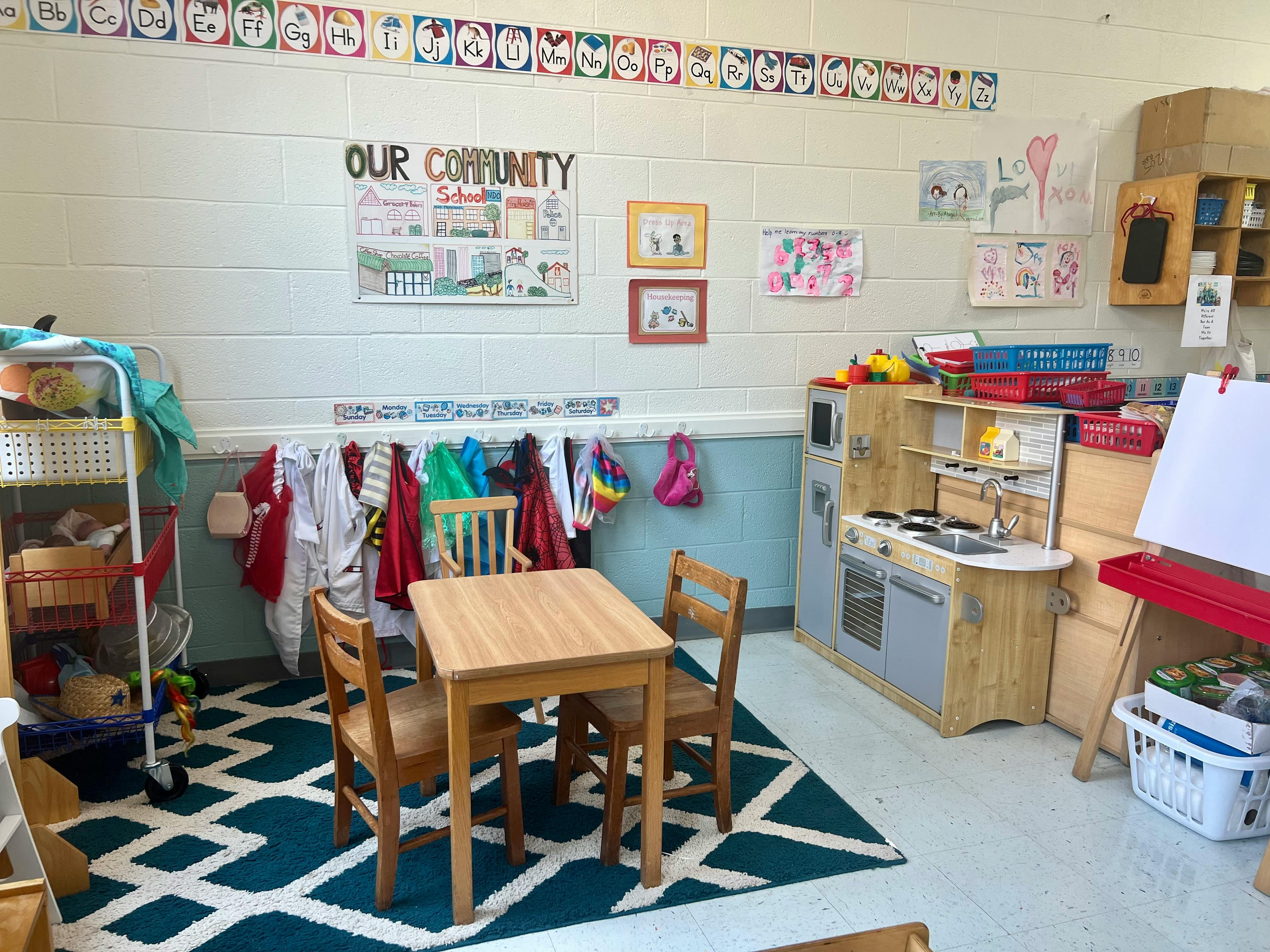 Classroom with small table and chairs, play kitchen, and coats hanging