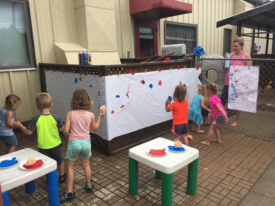 Children playing with paint on a white sheet outdoors