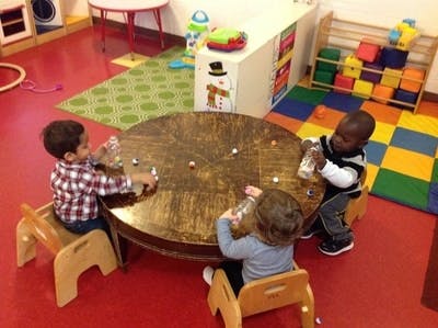 Three children playing with bottles around a round table in a classroom