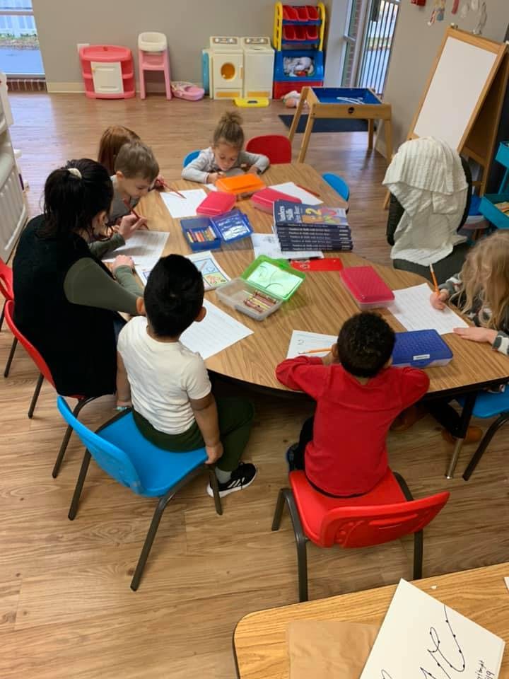 Adult and children drawing at a round table in a classroom