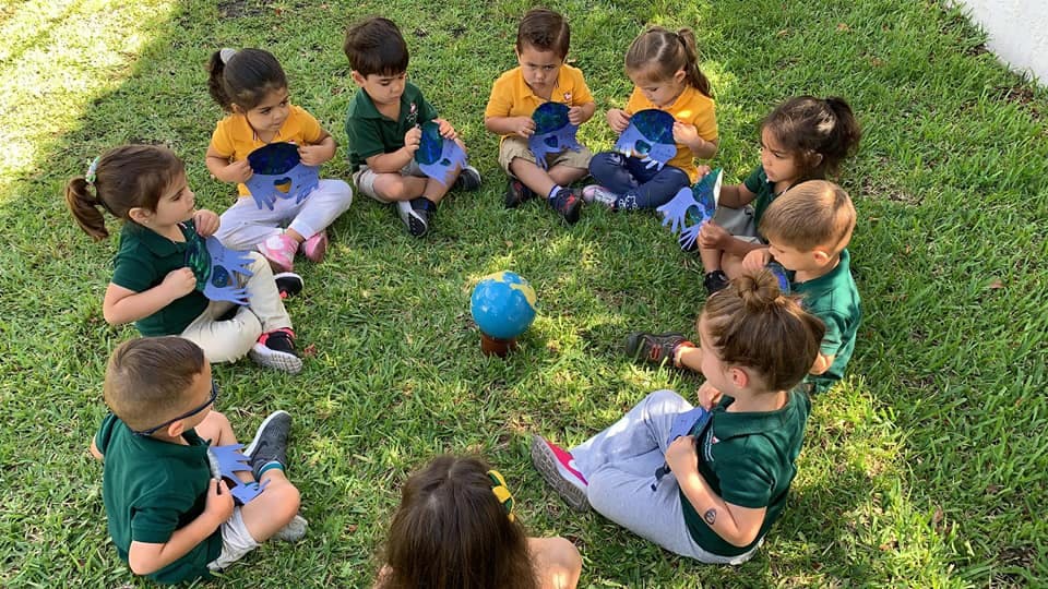 Children sitting in a circle on grass with a globe in the center