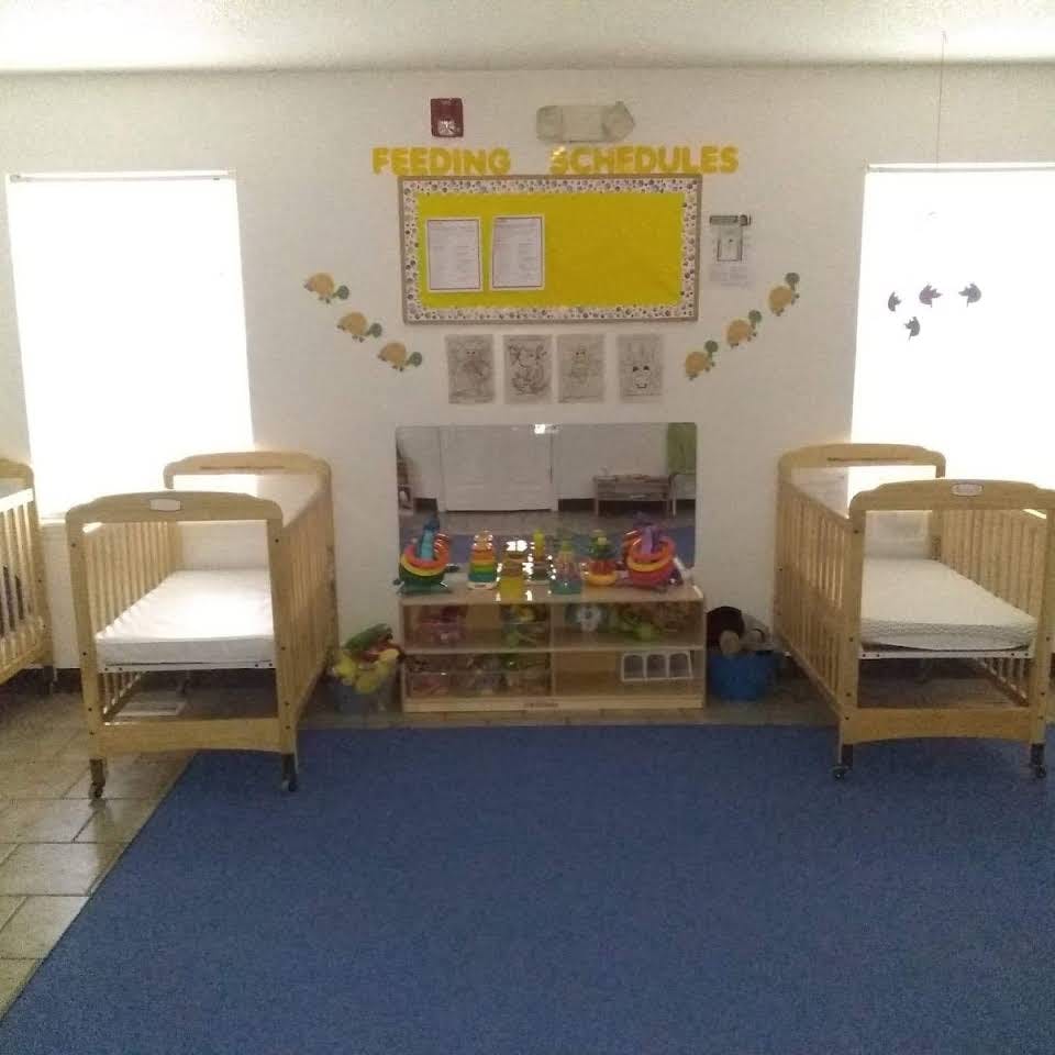 Two cribs in a room with a blue rug and a shelf of toys