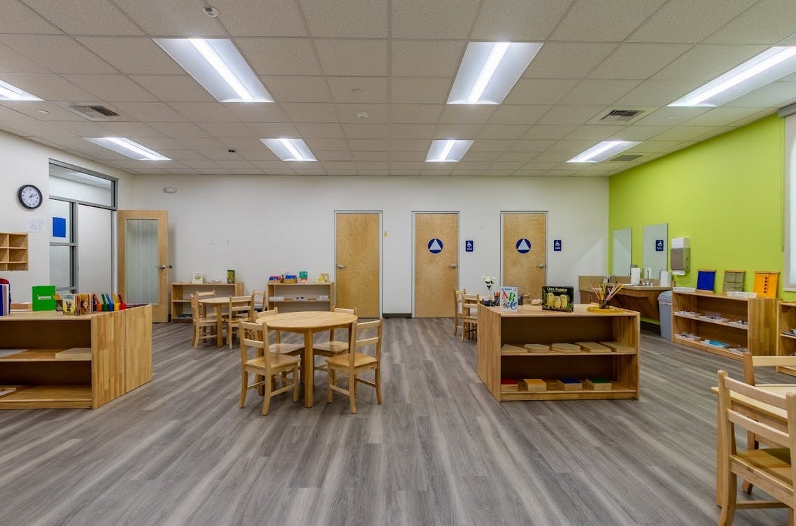 Empty classroom with small tables and chairs, shelves with learning materials