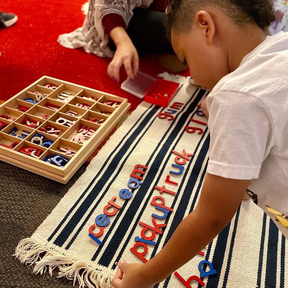 Child arranging letter tiles on a striped mat with words like "ice cream"