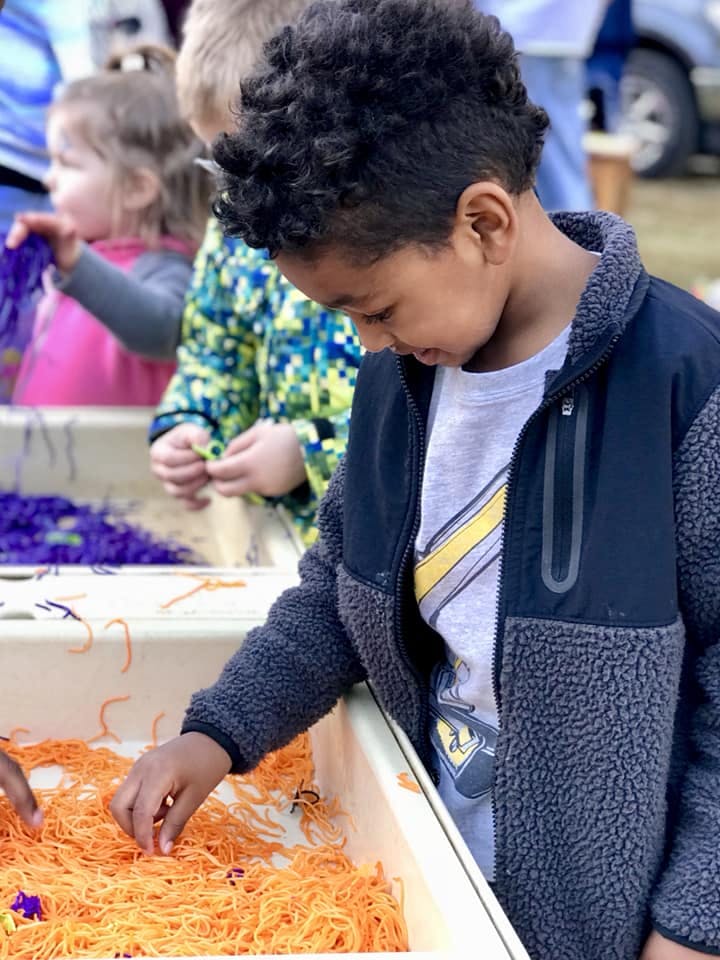 Child playing with orange string-like material in a bin