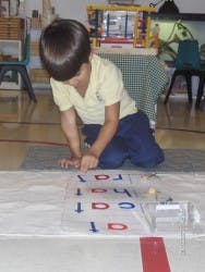 Child kneeling and pointing at letters on a mat