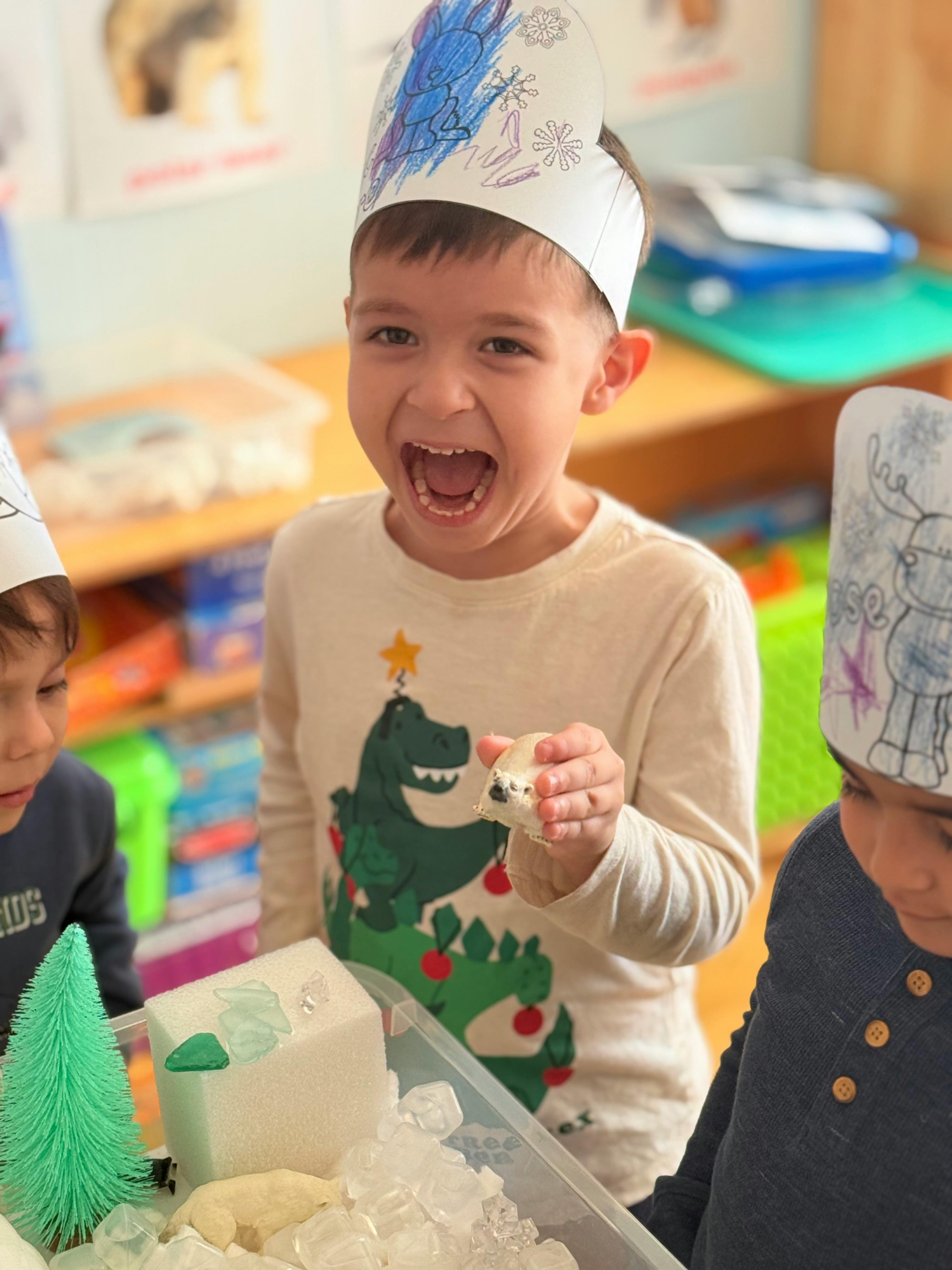 Child in a paper crown holding a small toy, mouth open
