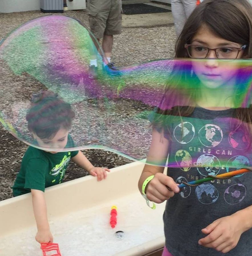 Child and teen making large bubbles outdoors
