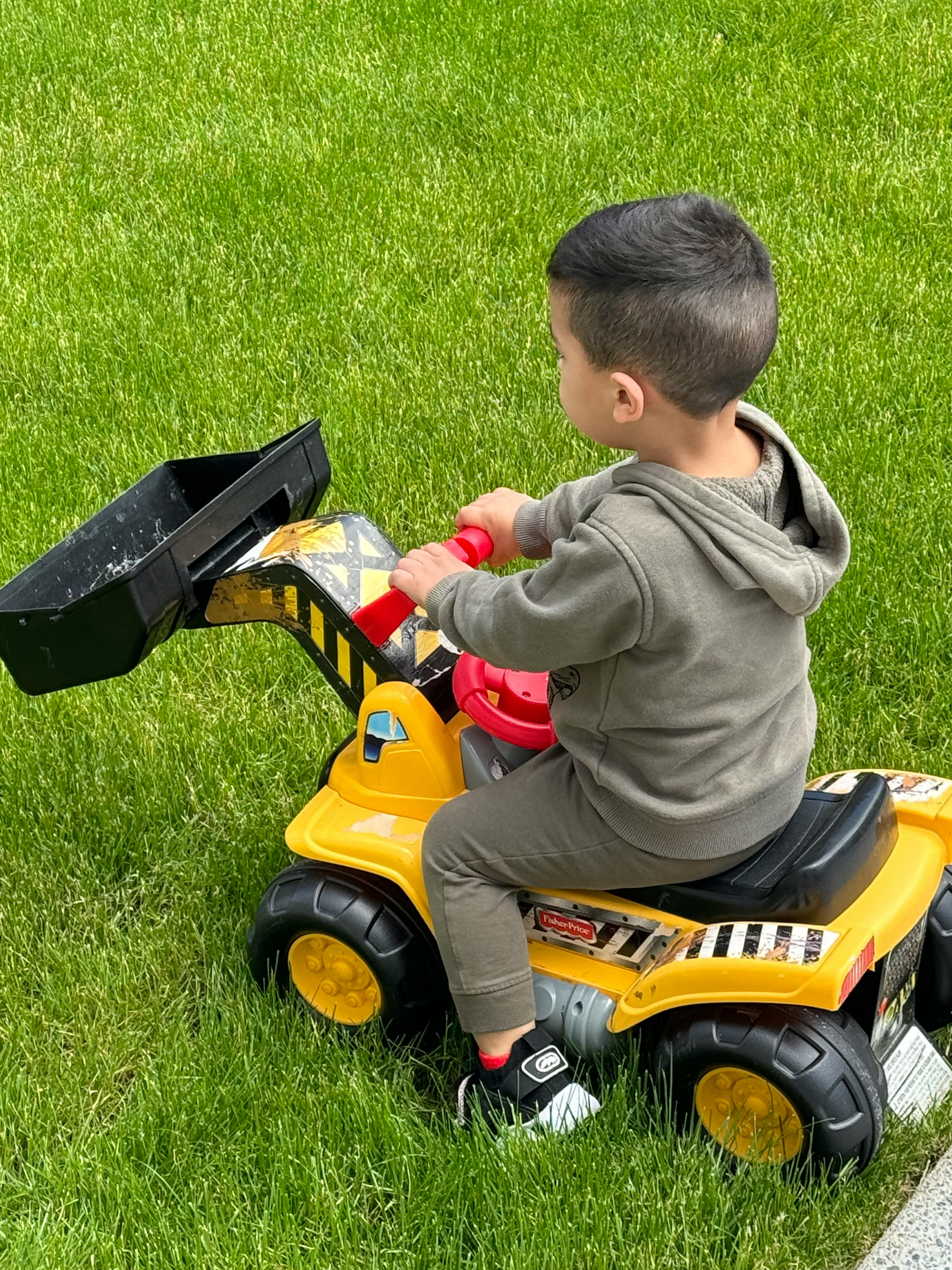 Child on a yellow toy construction vehicle in grass