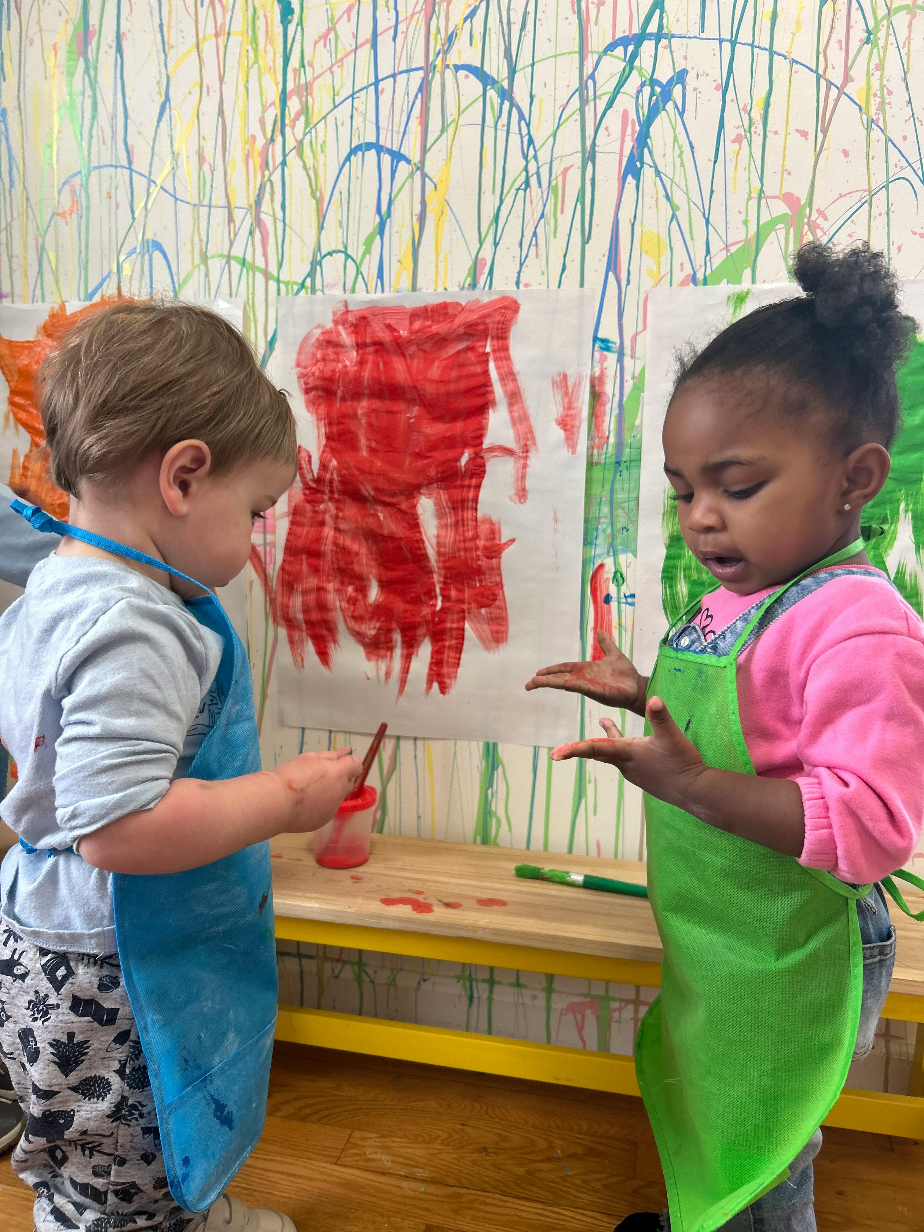 Two children in aprons painting at a table in a classroom