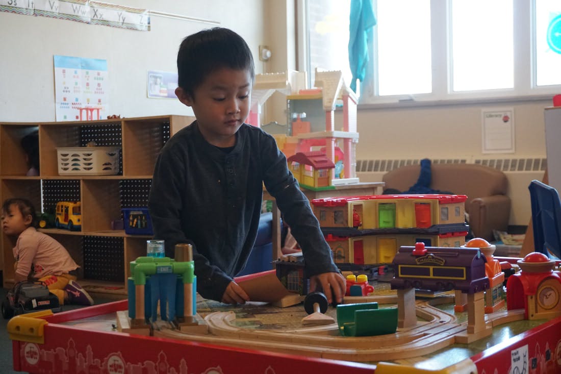Child playing with a toy train set in a classroom