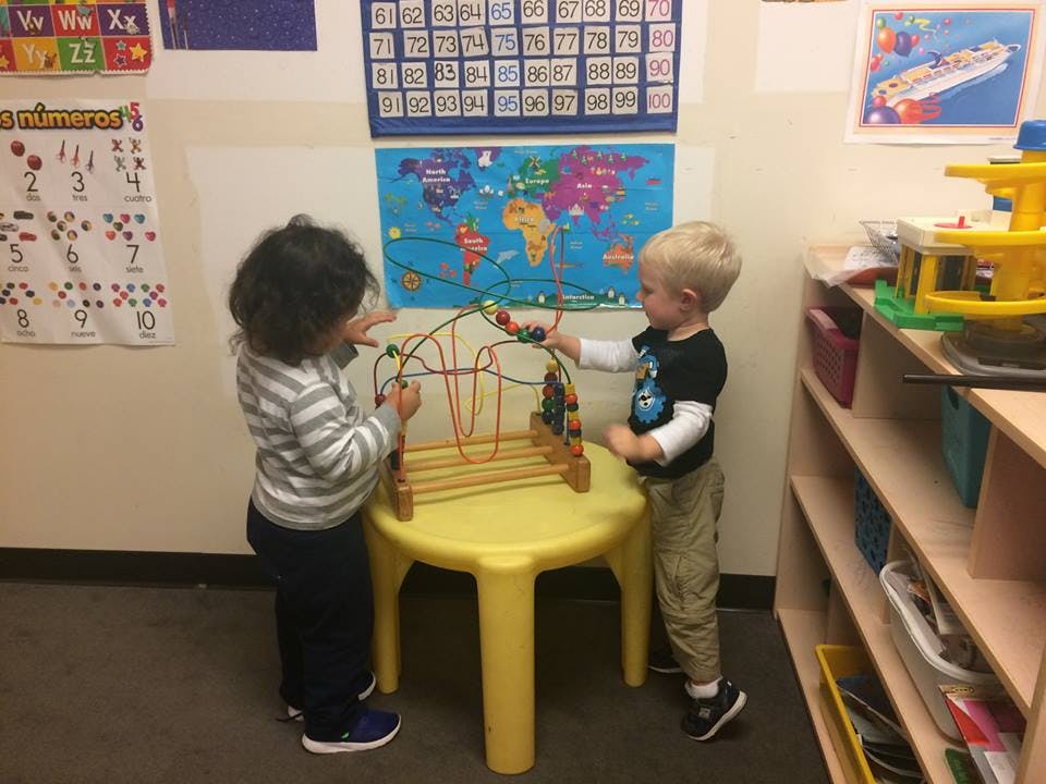 Two children playing with a bead maze on a yellow table in a classroom