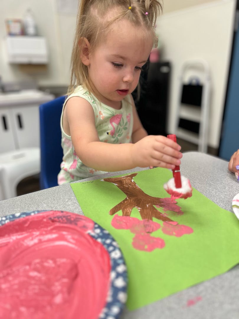Child painting a tree on green paper
