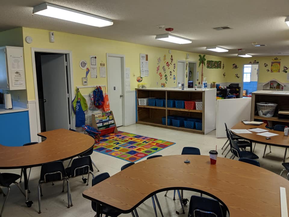 Classroom with small tables and chairs, colorful rug, and shelves