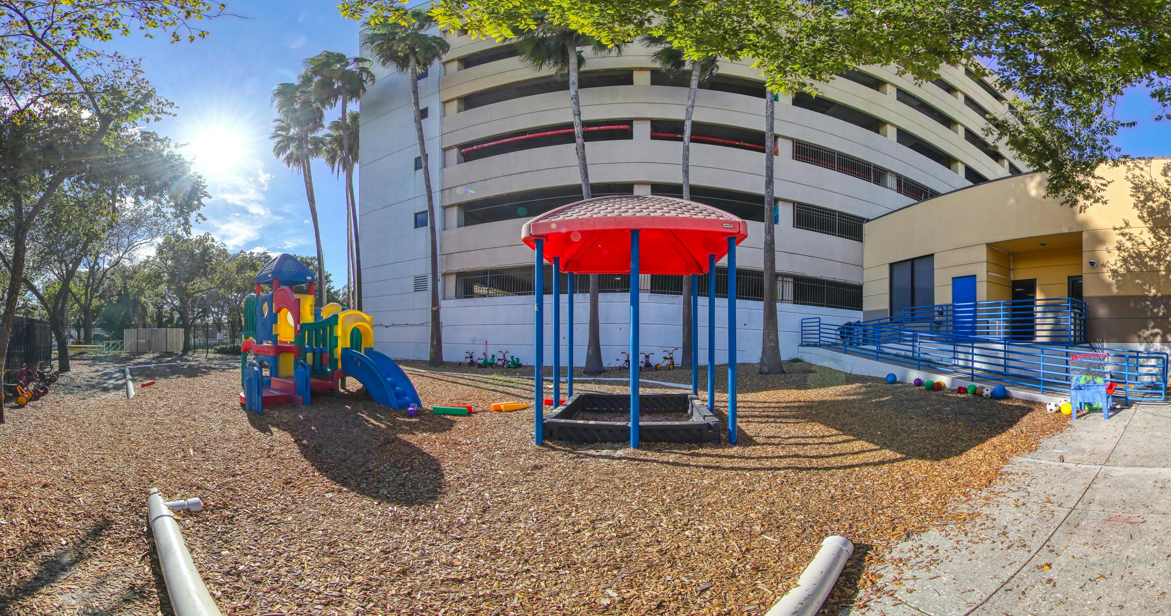 Playground with colorful equipment on wood chips next to a parking garage