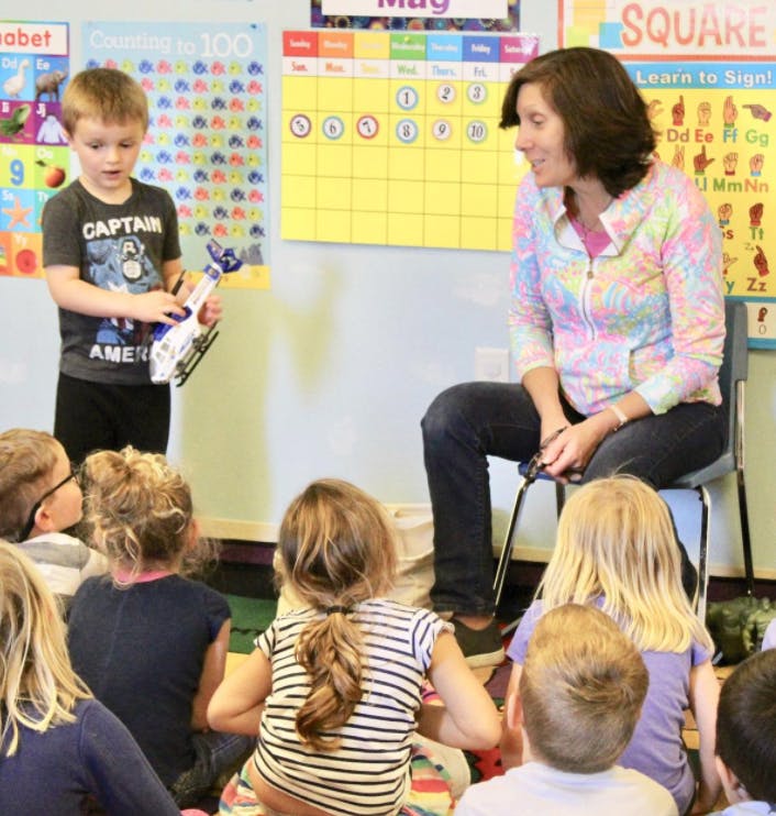 Child holding a toy helicopter in front of an adult and other children