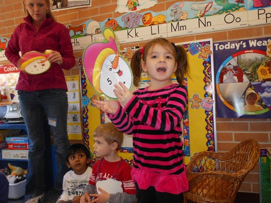 Child speaking in front of other children and an adult in a classroom