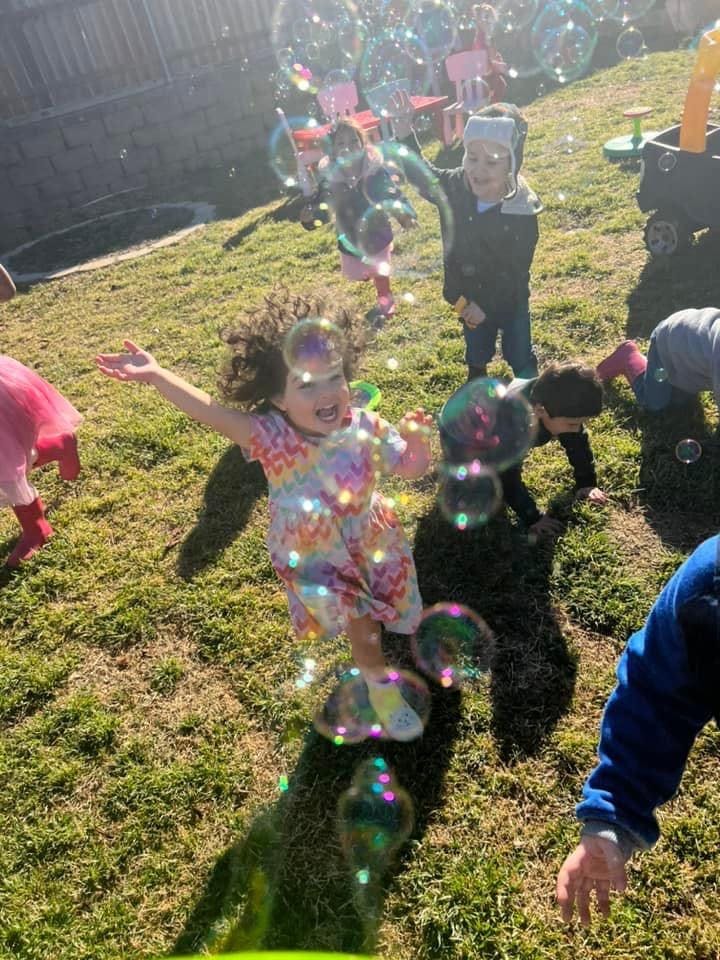 Child with open arms surrounded by bubbles outdoors