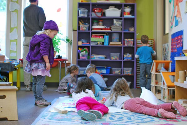 Children playing in a classroom, one child lying on the floor drawing