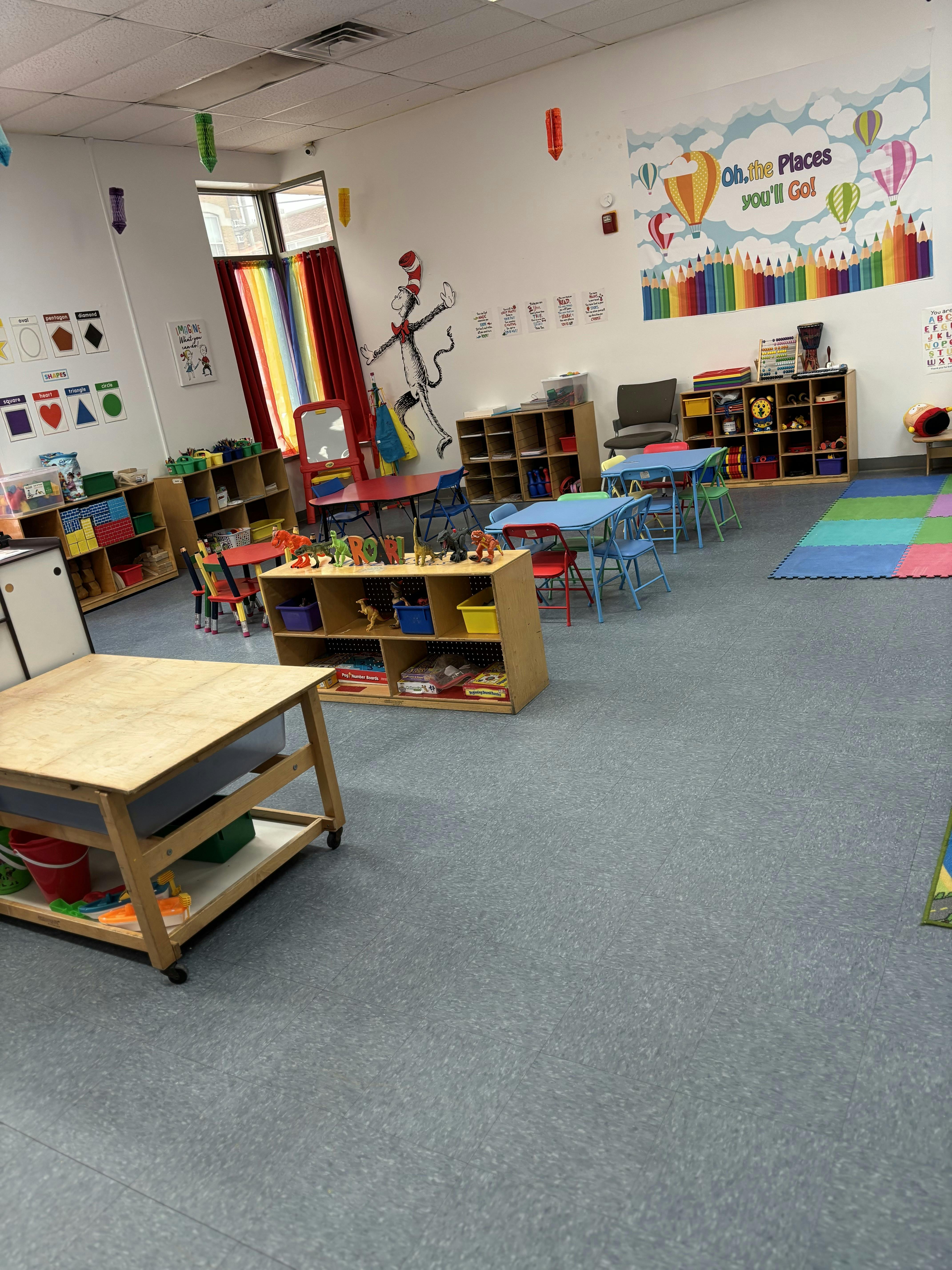 Classroom with small tables and chairs, shelves with toys, and wall decorations
