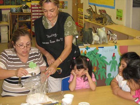 Two people and three children at a table, one person pouring from a bag