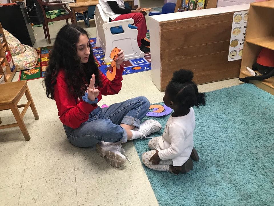 Person sitting on floor showing a child an orange letter