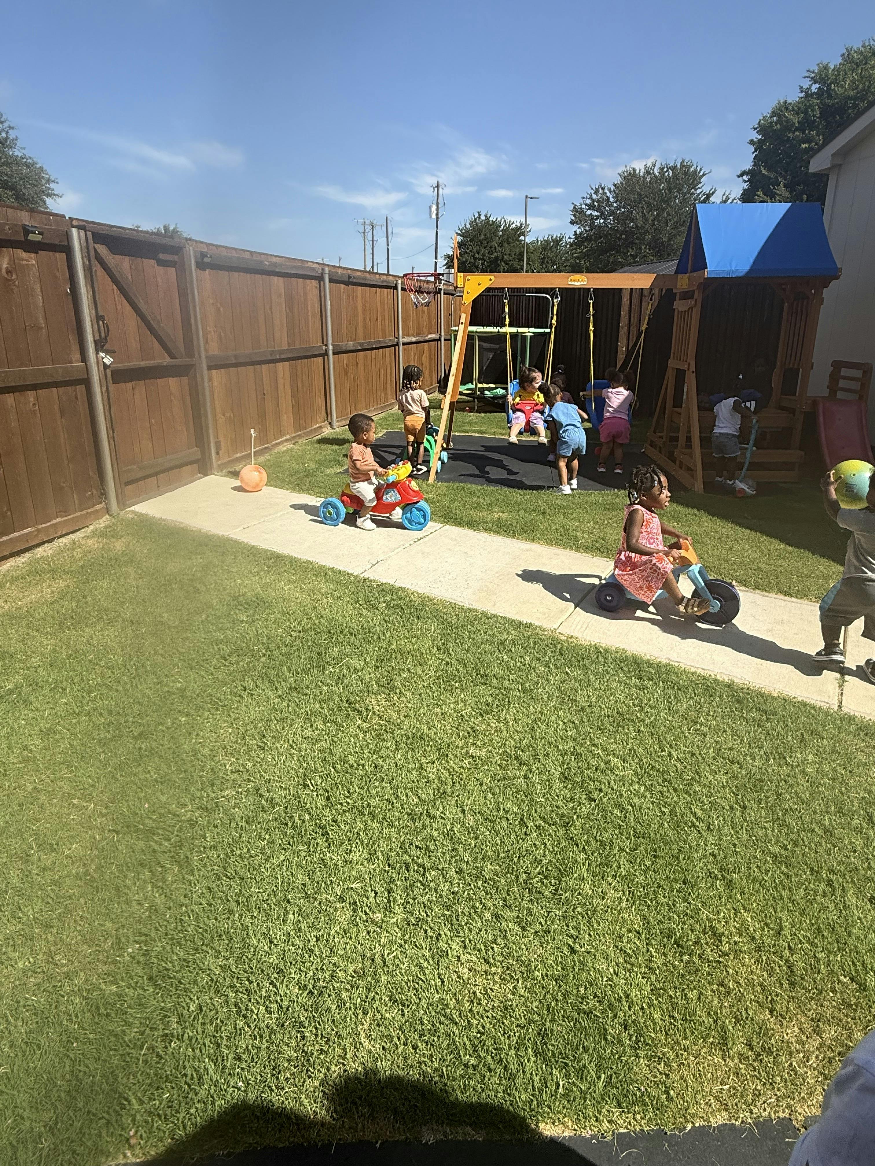 Children playing on tricycles and swings in a backyard