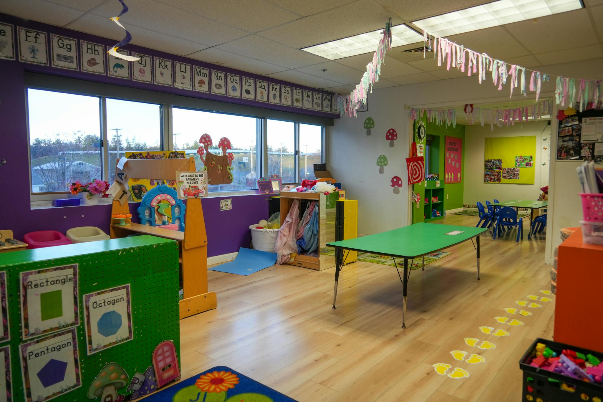 Colorful preschool classroom with tables, learning posters, and play areas