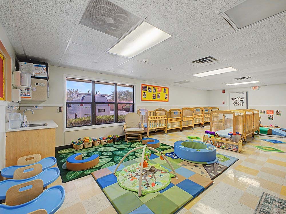 Infant classroom with cribs, playmats, activity gym, and a window