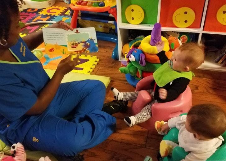 Person reading a book to two children in a play area