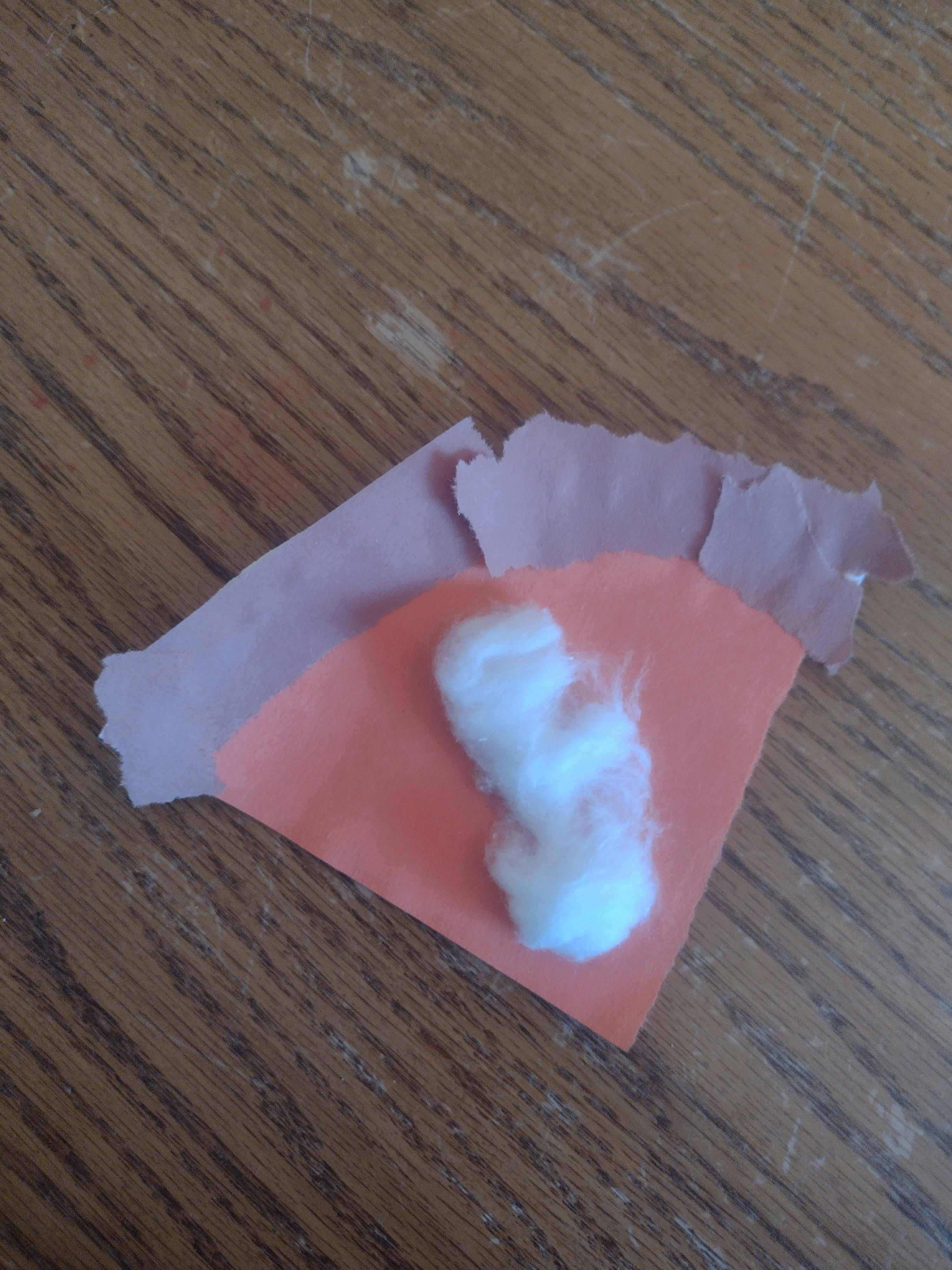 Cotton ball on orange paper with torn brown paper underneath