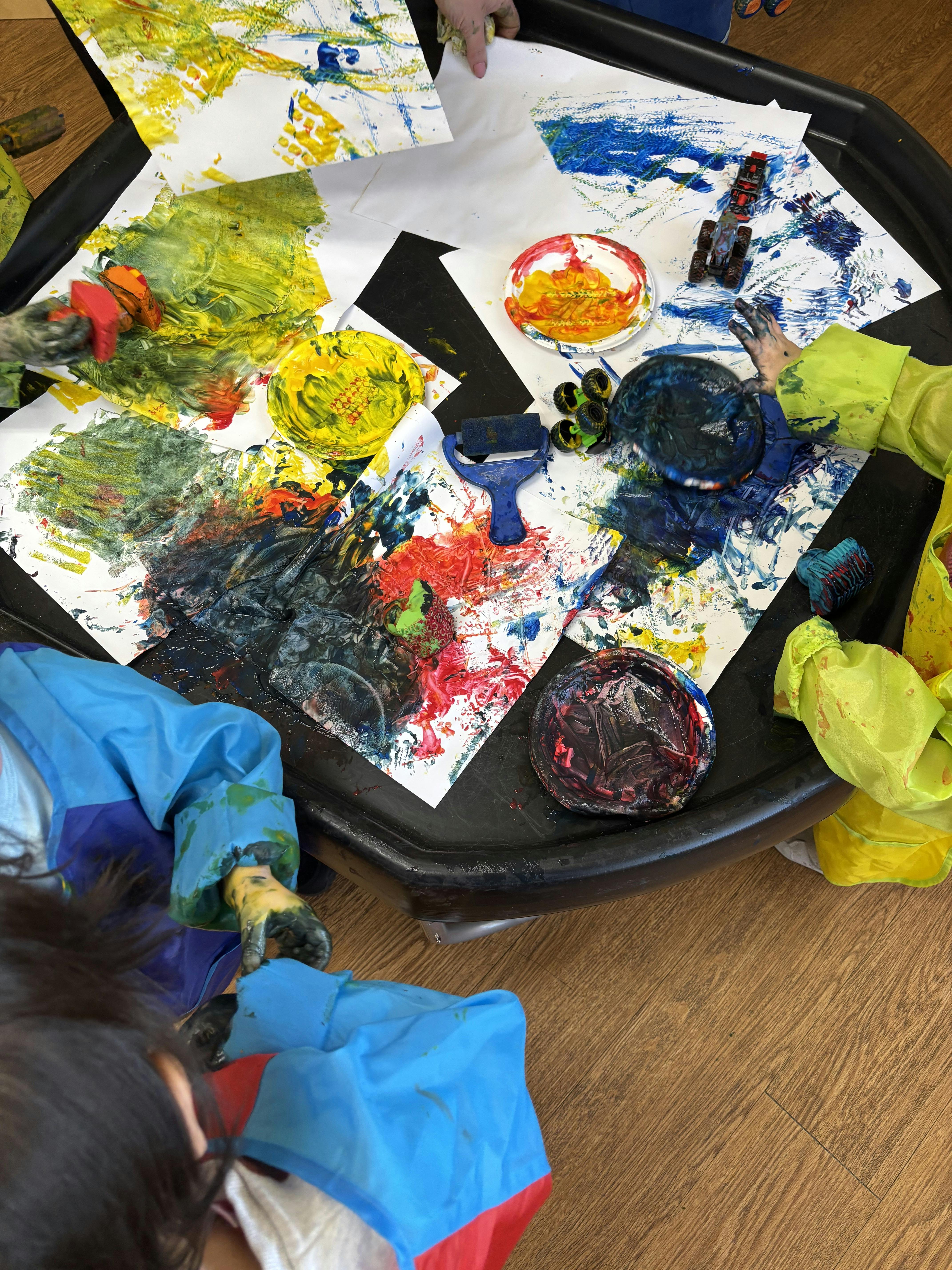 Children painting with hands and tools on a black tray with various colors