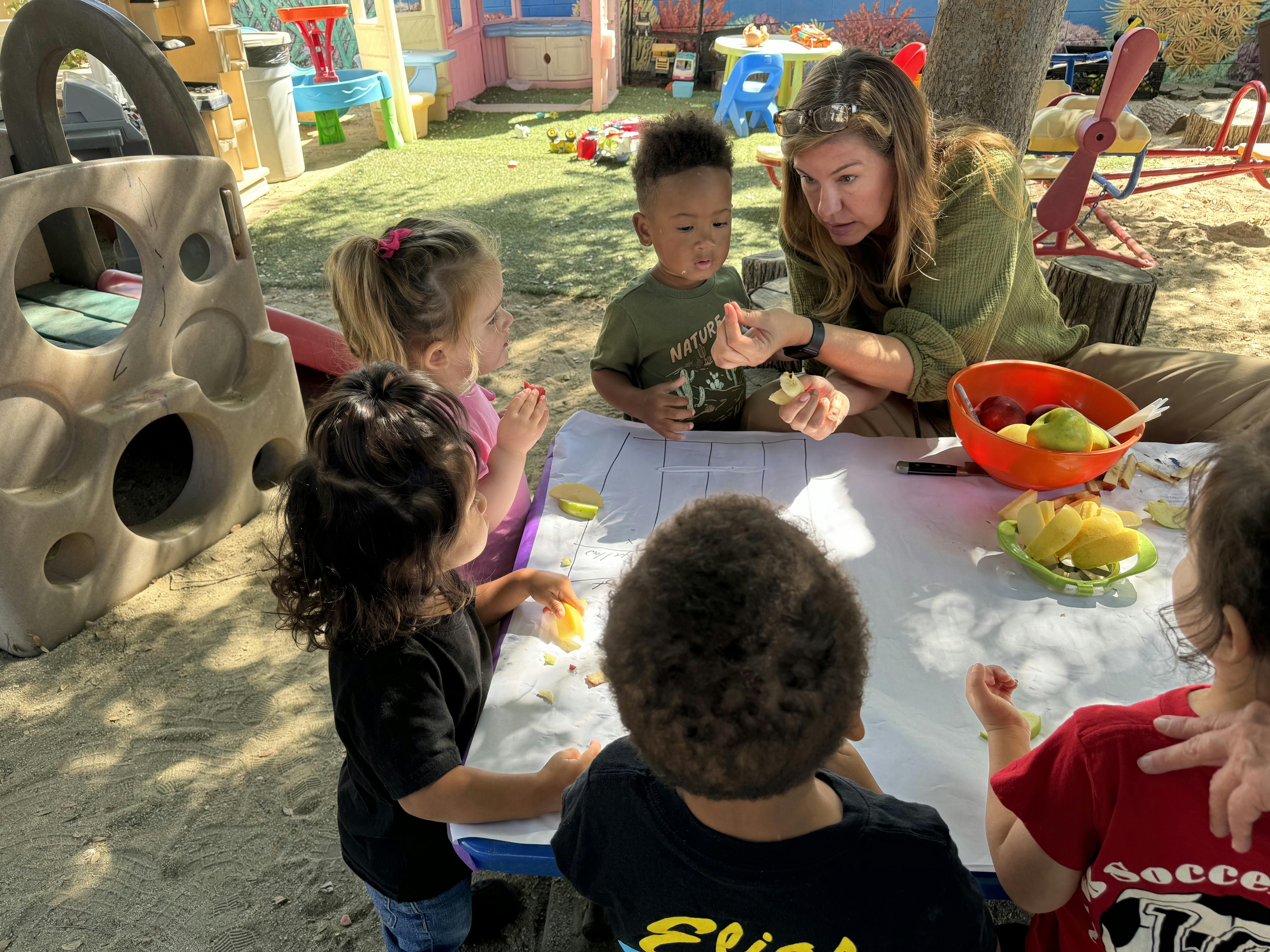 Adult with several children eating sliced apples at a table on a playground