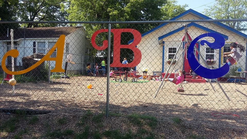 Large ABC letters on a chain link fence in front of a building with children