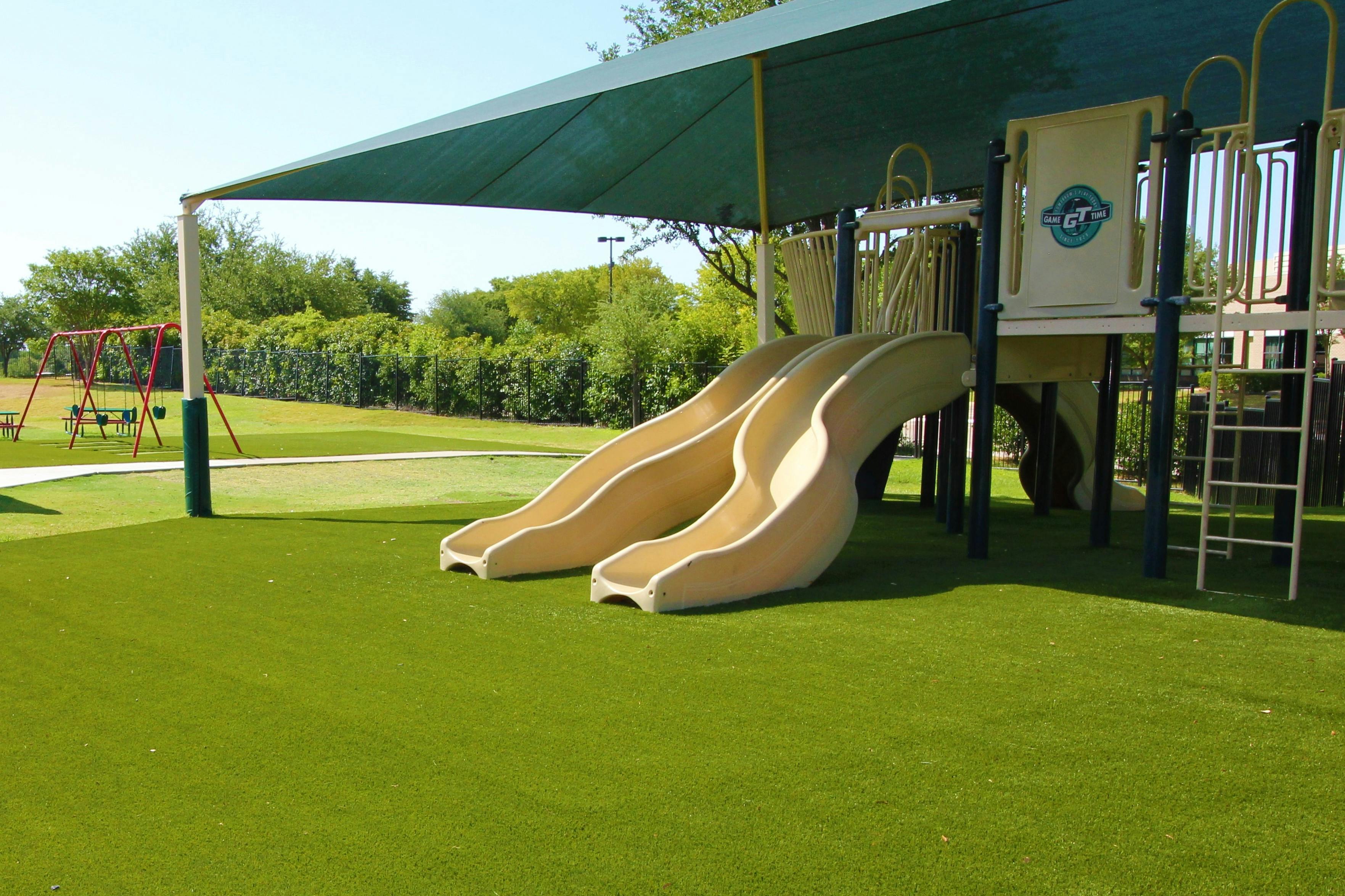 Playground with two slides and a climbing structure under a shade canopy
