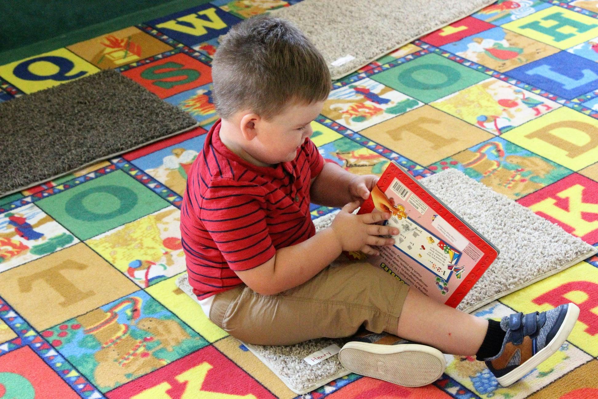 Child sitting on an alphabet rug, holding a book