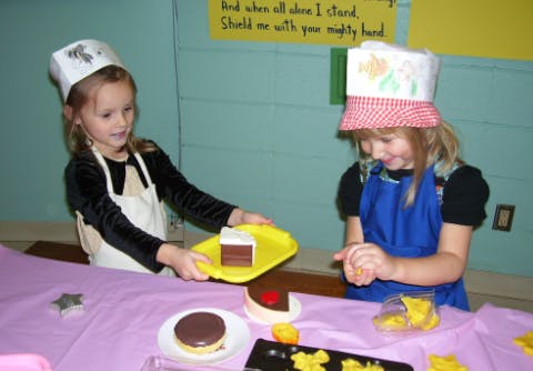 Two children playing with toy food, one holding a tray with cake
