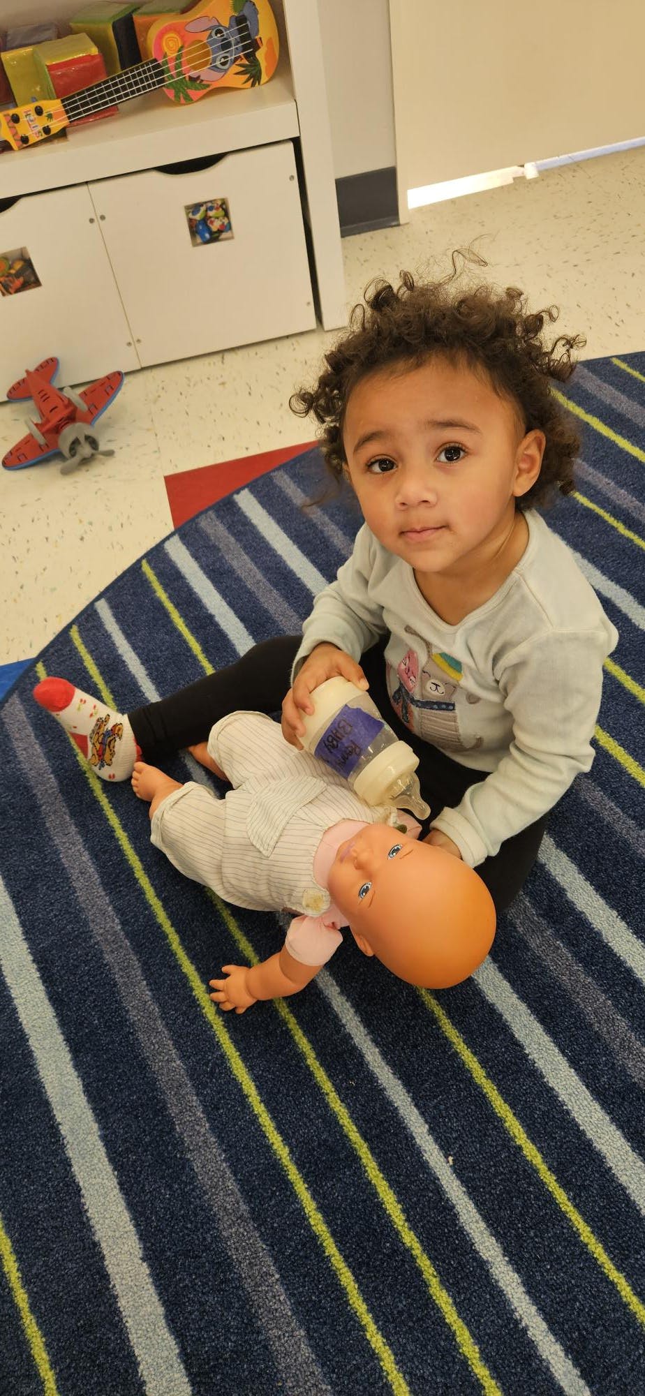 Child feeding a baby doll with a bottle on a striped rug
