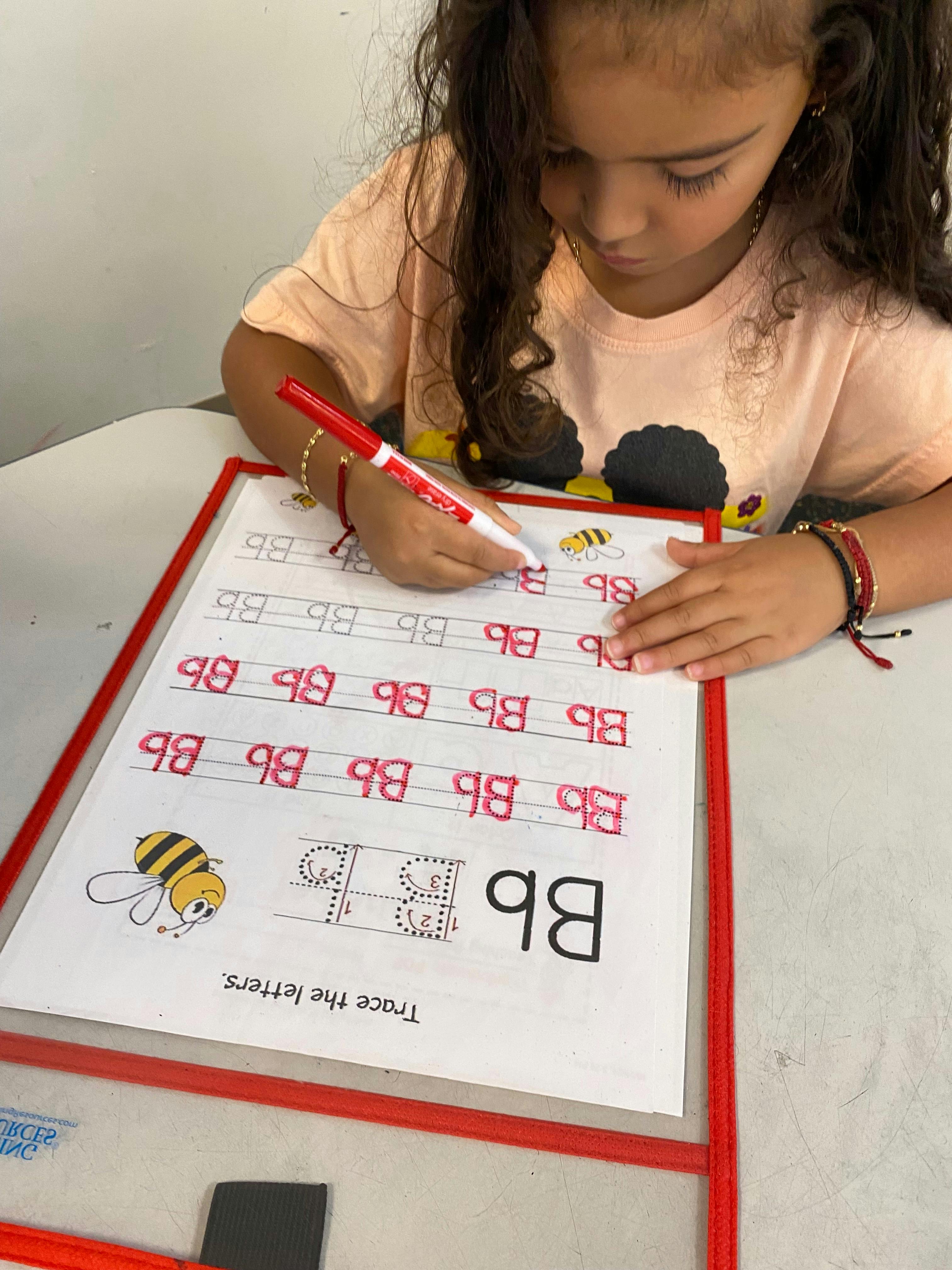 Child tracing letters on a worksheet with a red marker