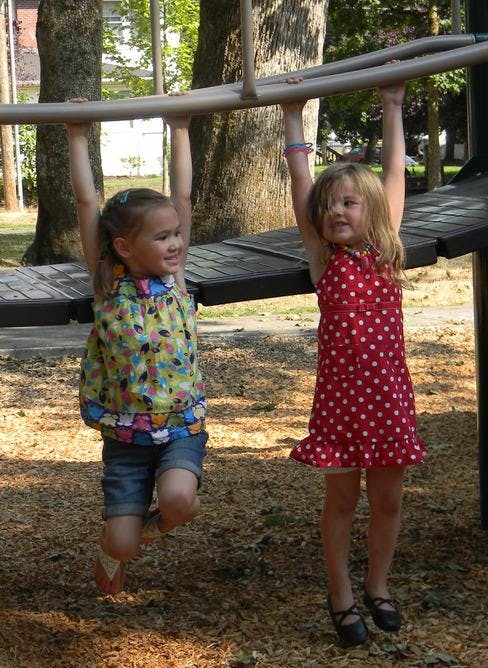 Two children hanging from monkey bars on a playground