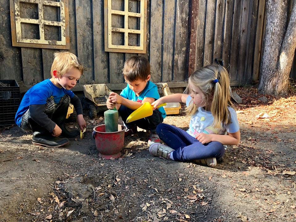 Three children playing in dirt with shovels and buckets