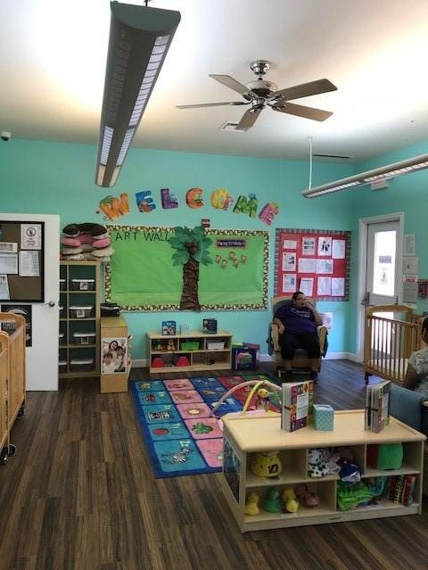 Classroom with colorful rug, cribs, and a person sitting in a chair