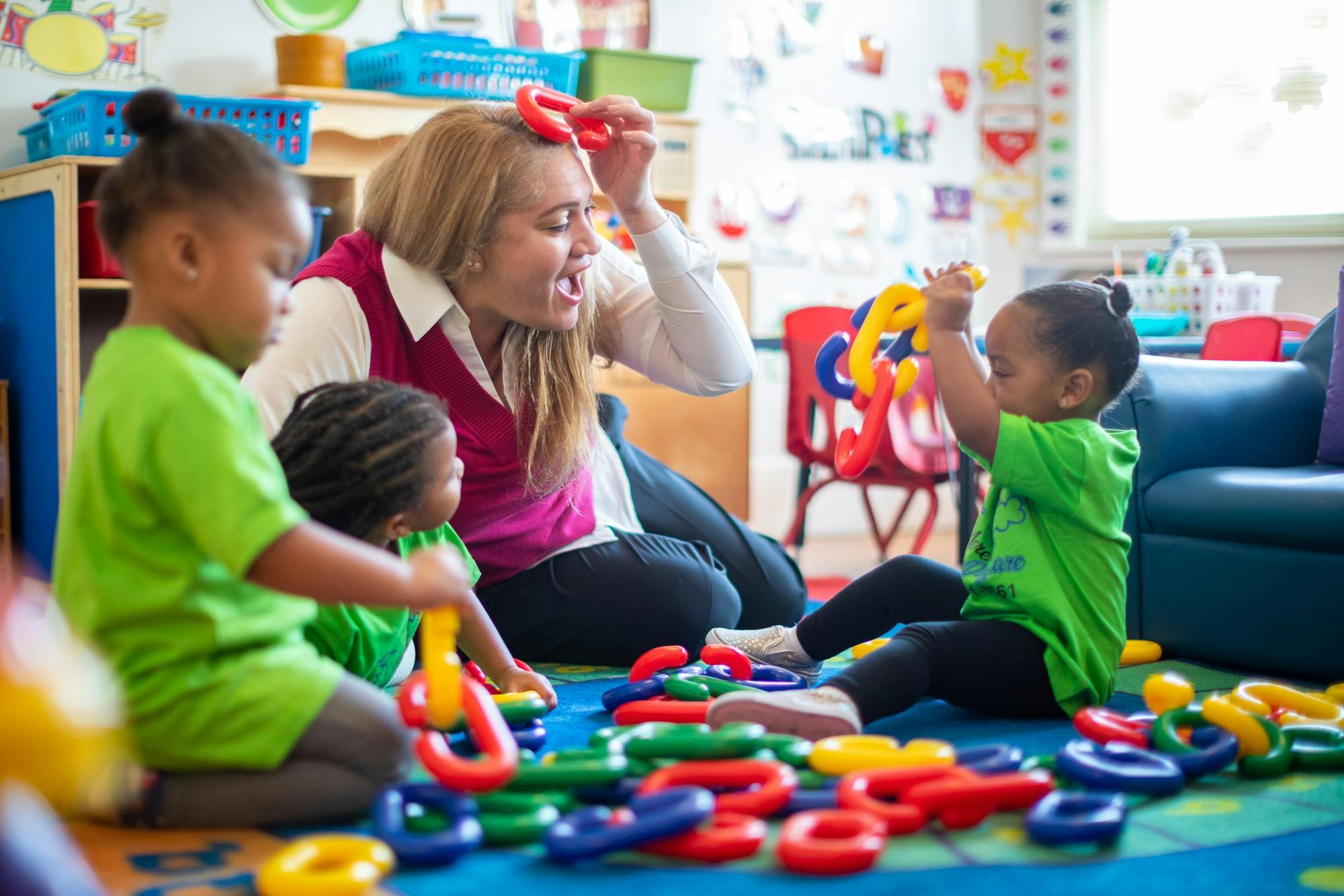 Adult and two children on floor playing with colorful linking toys in a classroom