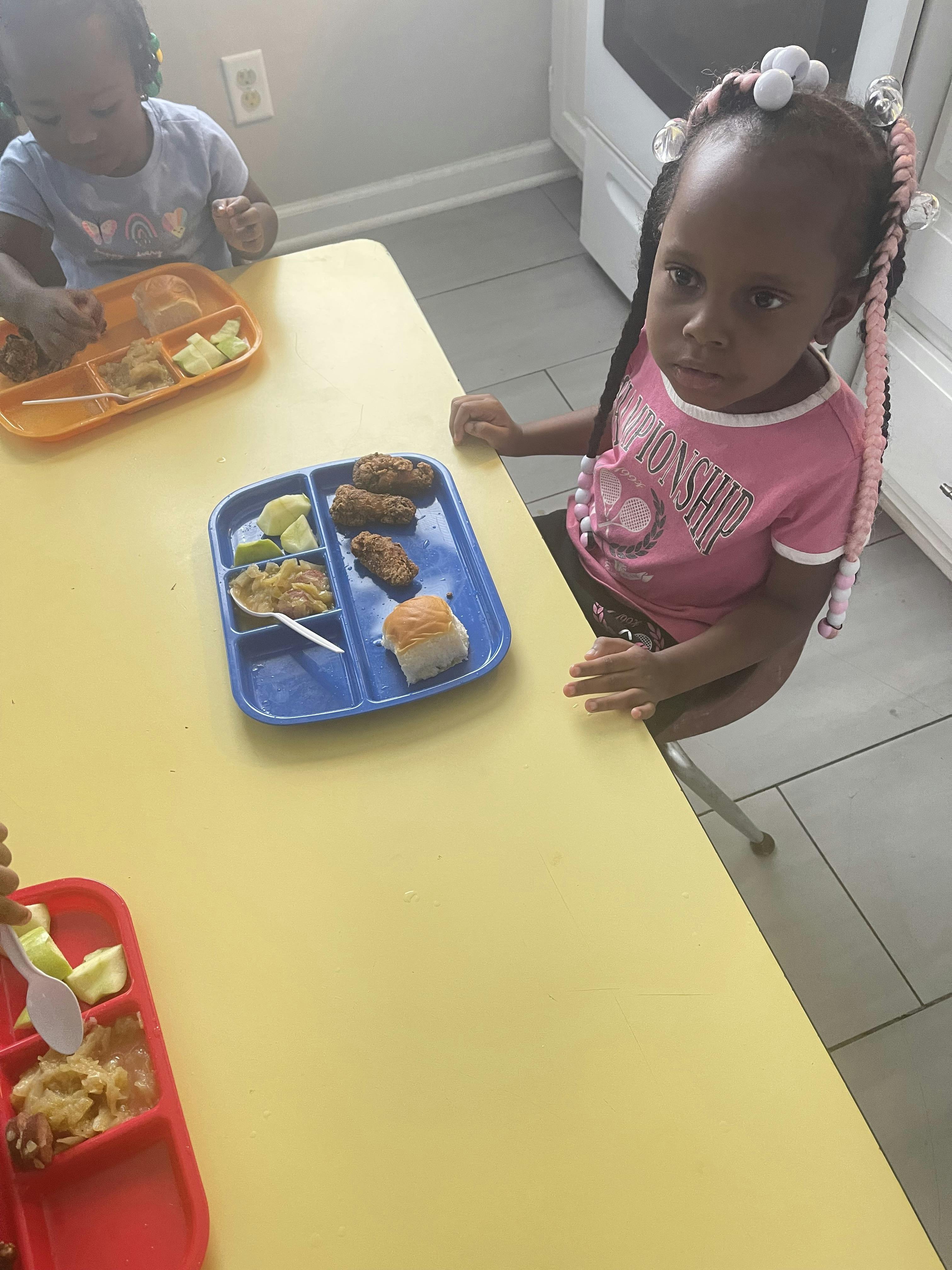Child sitting at a yellow table with a meal tray