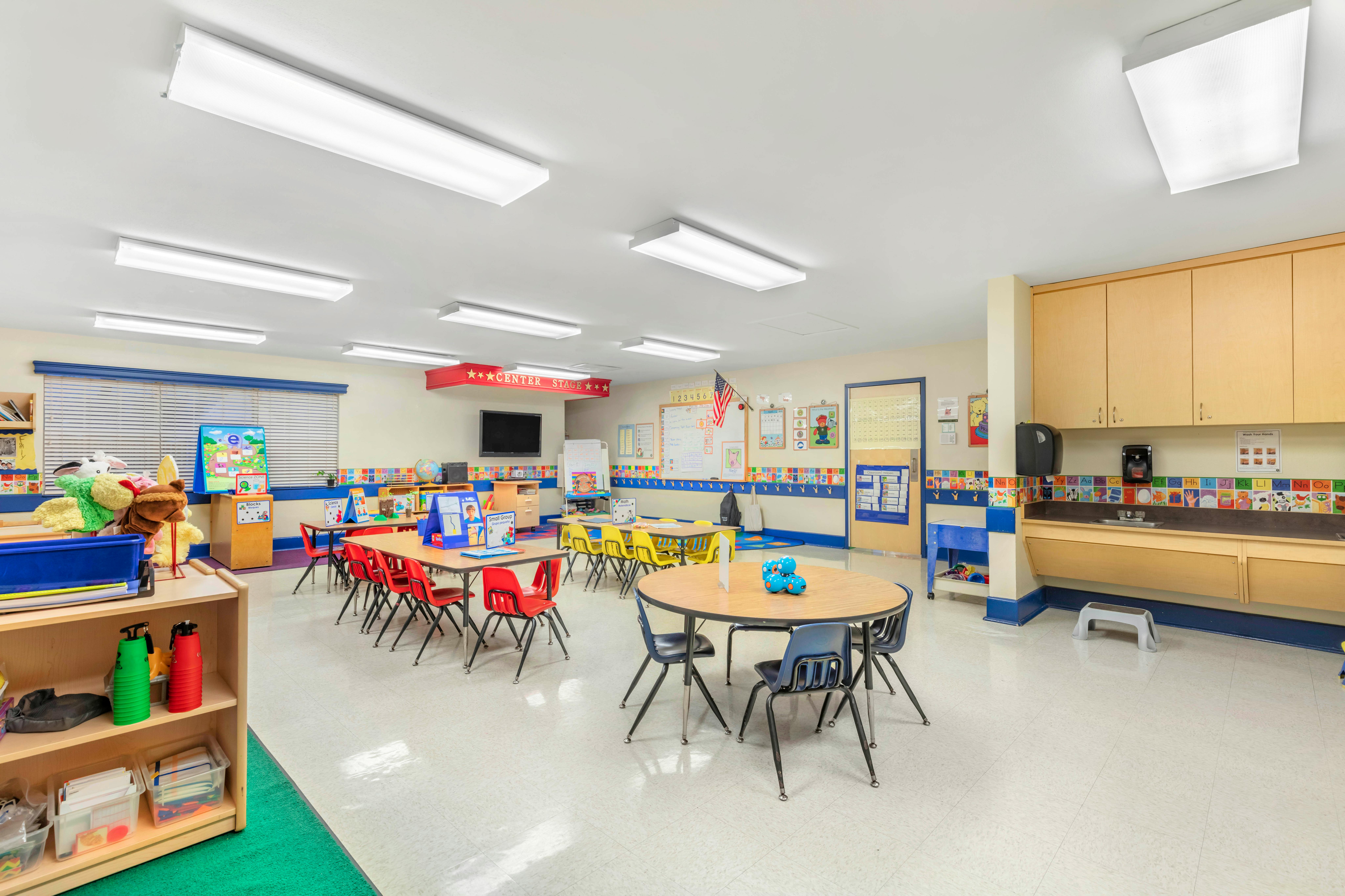 Classroom with small tables and chairs, a sink, and educational decorations