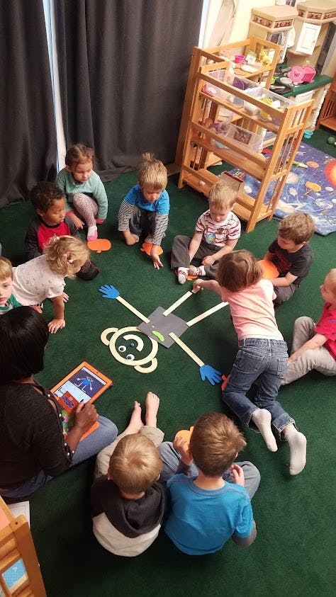 Teacher and children creating a person shape out of craft supplies on the floor
