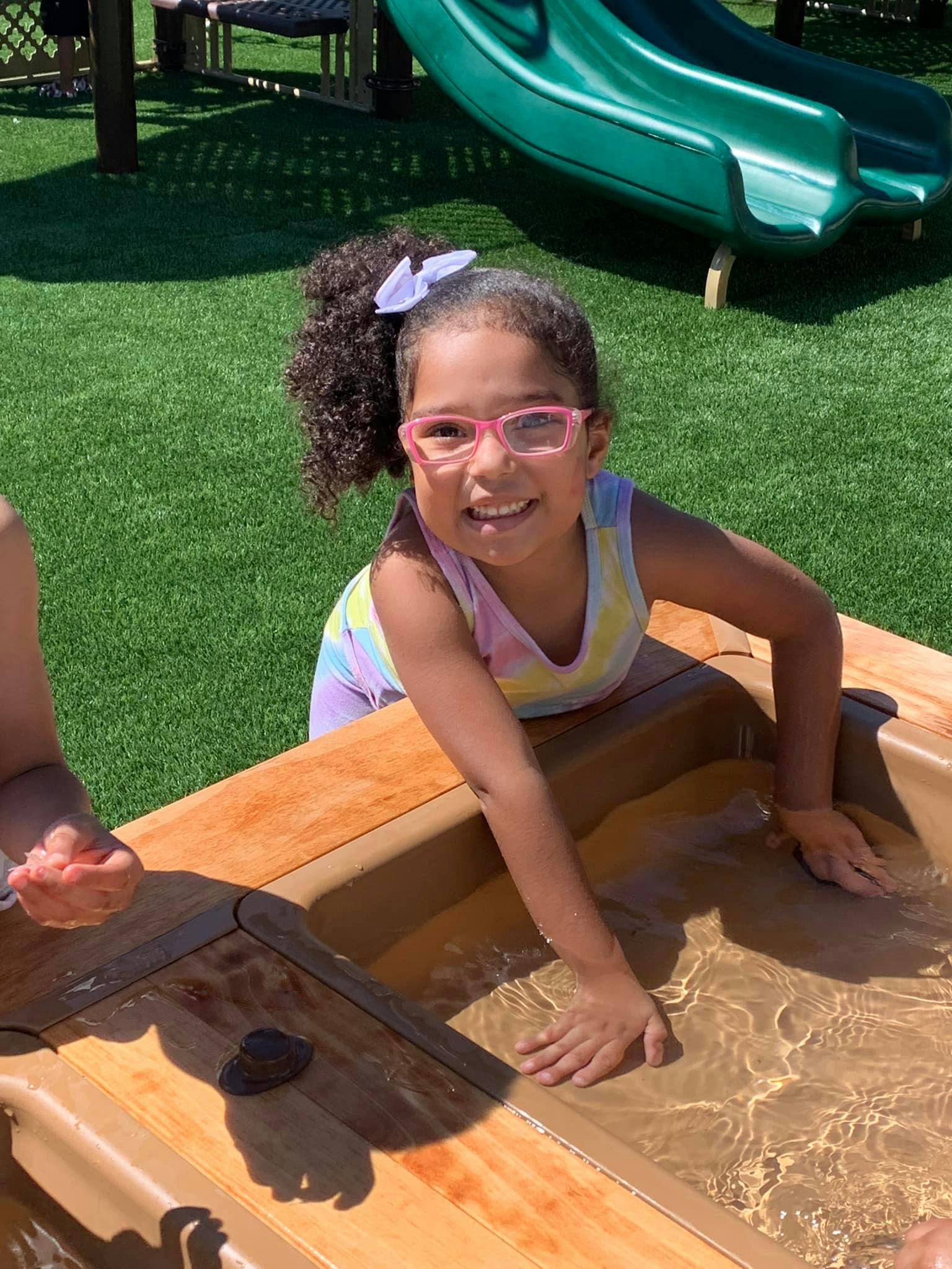 Child with pink glasses playing in a water table