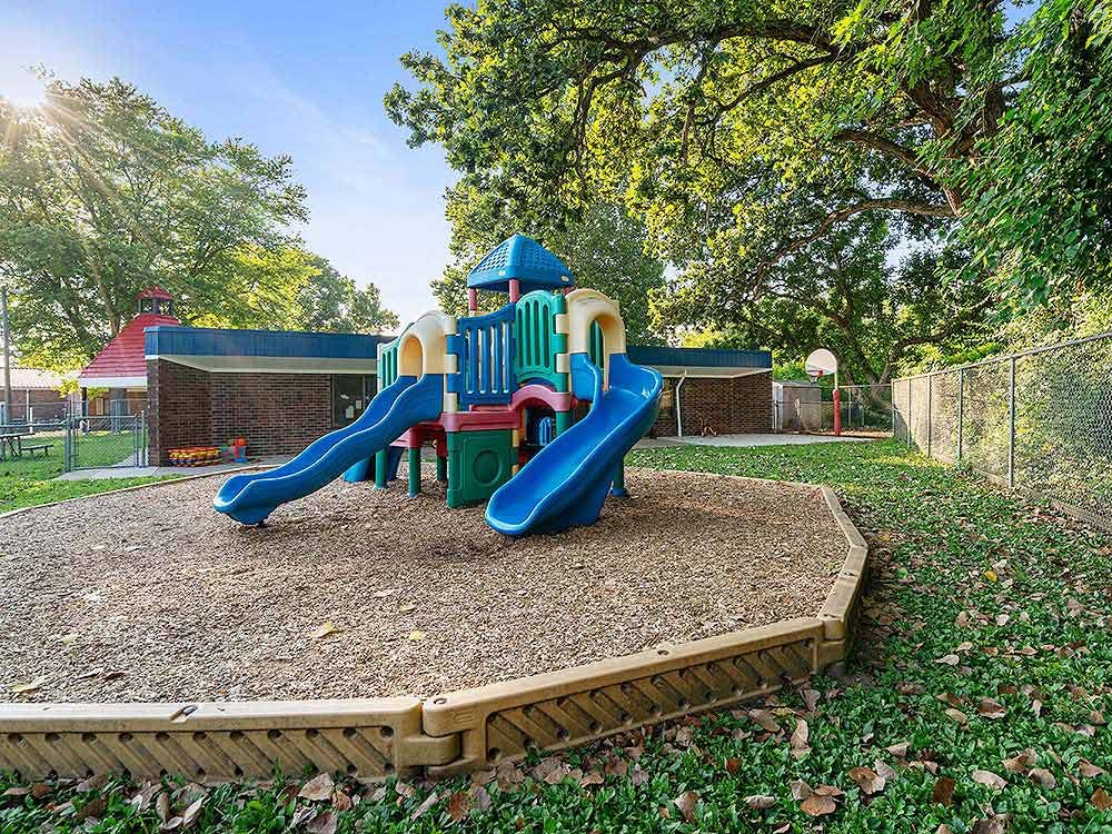 Colorful playground structure with slides on wood chips, next to a building