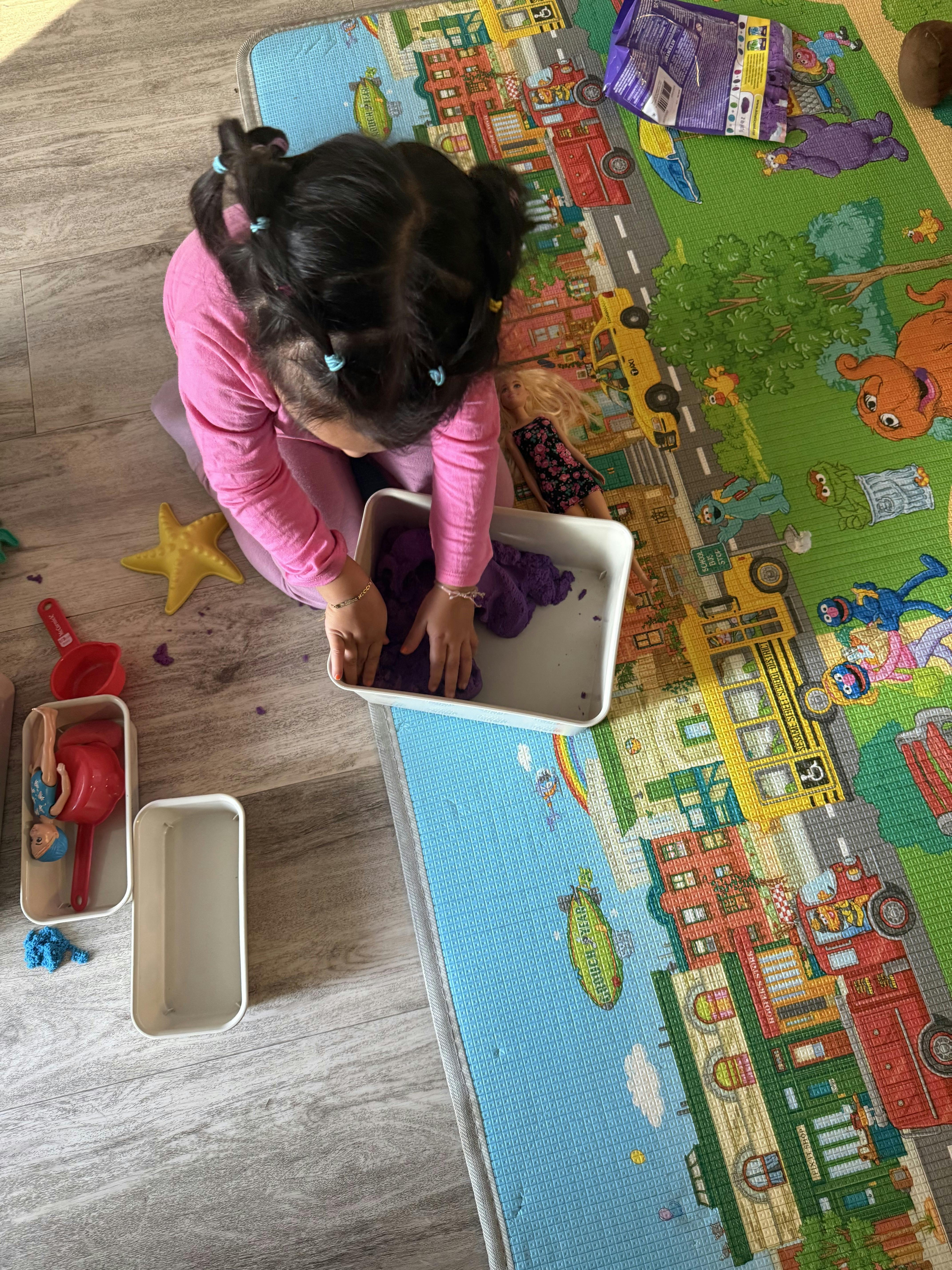 Child playing with purple sensory dough in a tray on a printed floor mat