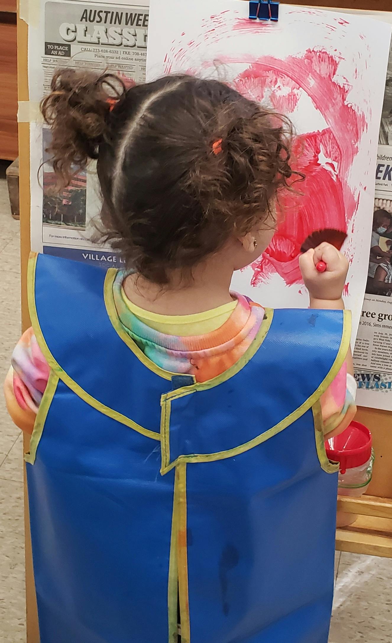 Child in smock painting with red paint on an easel